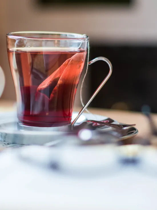 Glastasse mit Schwarzem Tee und Teekanne auf Holztisch neben Buch und Brille